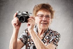 reife Dame hält einen Fotoapparat in den Händen und lacht | © istock-tatyanagl_58210034